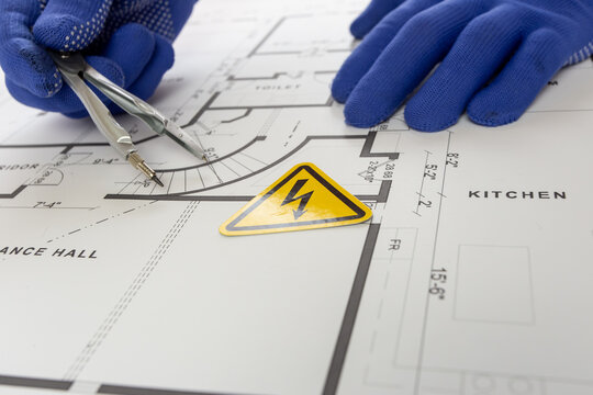 Mark the high-voltage area on the drawing with a warning sign. An electrical engineer takes measurements on the drawing using a pair of dividers.