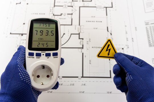 A worker holds a portable multimeter and a triangular high-voltage warning sign over a paper production plan.