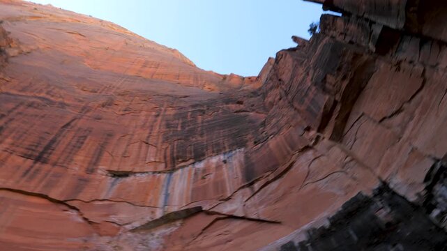 Majestic upward tilt revealing immense scale of sheer red sandstone cliff face within a narrow canyon, culminating in a view of the bright blue sky above towering rock formations in Zion national park