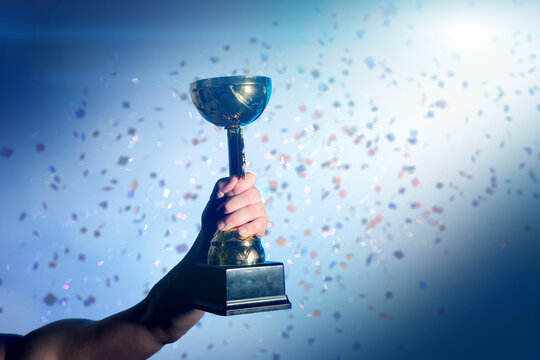 Hand Raising Golden Trophy  cup  with Falling Confetti Background