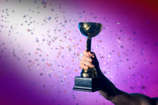 Hand Raising Golden Trophy with Falling Confetti Background