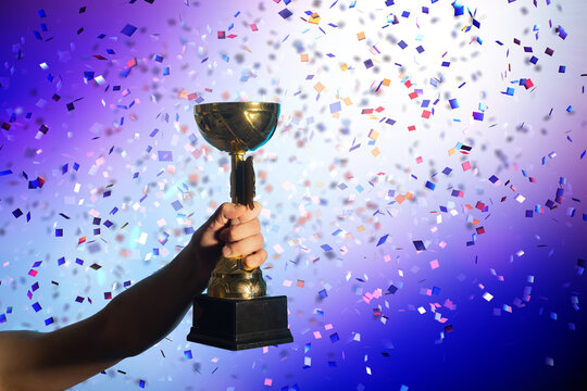 Hand Raising Golden Trophy with Falling Confetti Background