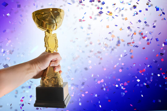 Hand Raising Golden Trophy  cup  with Falling Confetti Background