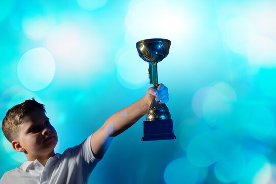 Boy Celebrating with Golden Trophy and Confetti on Blue Background