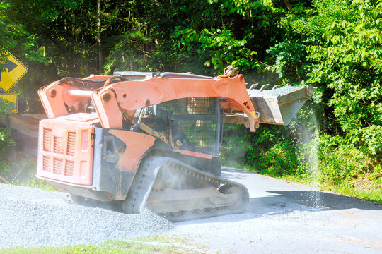 Construction equipment spreads gravel on road near curve in wooded area