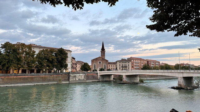 Urban river bridge and church spire framed by trees in Verona Italy