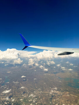 Aircraft wing with blue tip soaring above clouds and landscape, showcasing the vast sky and terrain below during a flight over a scenic region