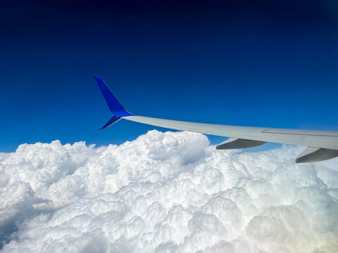 Aircraft wing extending over fluffy white clouds against a clear blue sky, showcasing the beauty of flight and the vastness of the atmosphere