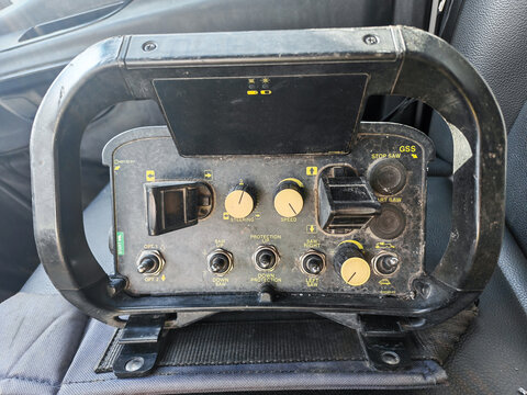 Control panel of an asphalt cutter featuring various knobs and switches, positioned on a textured seat inside a vehicle cabin