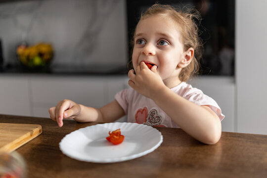 Young girl eating a cherry tomato at the kitchen table enjoying a healthy snack