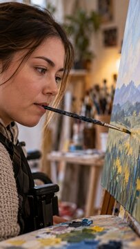 Disabled female artist in wheelchair painting on canvas using mouth