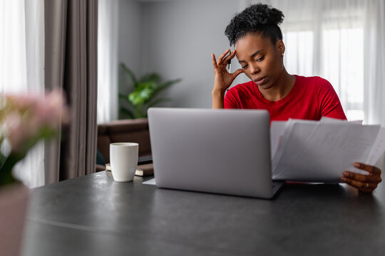 Woman working from home reviewing documents and using laptop at a table