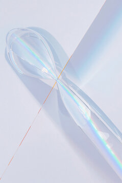 A transparent glass whisk casting a colorful prismatic rainbow shadow on a white surface, creating a delicate and abstract light refraction effect