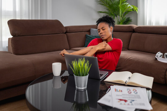Black woman stretching while working from home on laptop in living room sofa