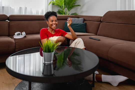 Smiling woman relaxing on couch eating popcorn while watching TV at home