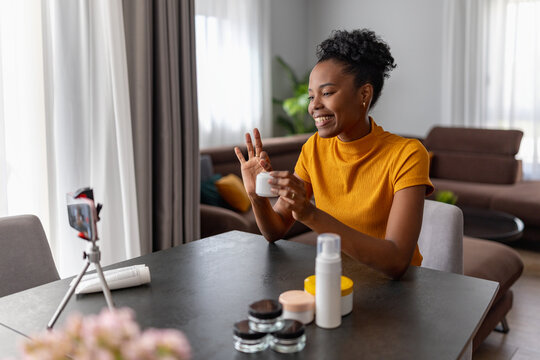 Young woman recording skincare product review at home with smartphone tripod and smile