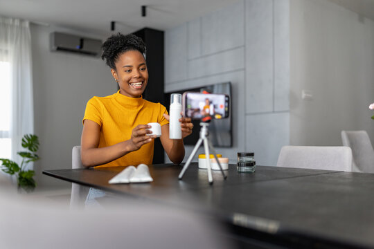 Woman demonstrating skincare products on smartphone for beauty vlog at home by black woman creator