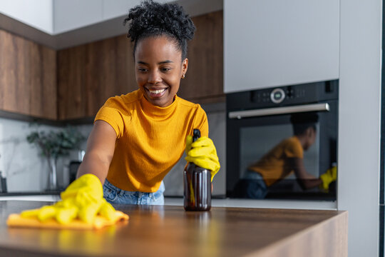 Black woman cleaning modern kitchen island with yellow gloves and a smile