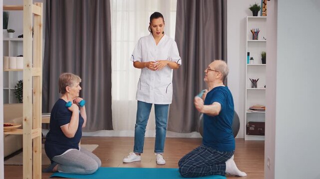 Older adults exercise on a yoga mat with dumbbells while a physiotherapist gives instruction, supporting strength, mobility and active aging at home.