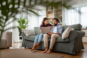 Couple relaxing on sofa at home using laptop in bright living room