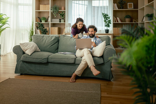 Couple relaxing on sofa at home using laptop and enjoying coffee while browsing together