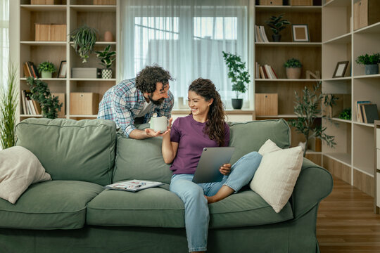 Young couple relaxing on sofa at home with tablet and coffee in cozy living room