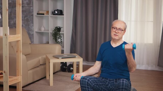 Senior man performs a focused single-arm dumbbell curl while seated at home, highlighting upper-body strength, controlled movement, senior fitness and active aging to support strength training.