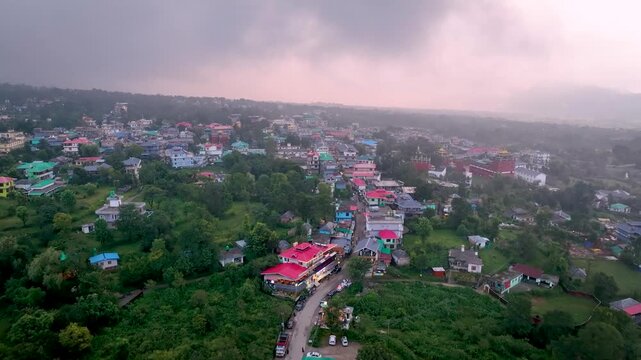 Aerial Flyover: Cinematic aerial drone flyover showcasing the sprawling town of Bir, colorful Himalayan rooftops, and misty mountain valleys in Himachal Pradesh