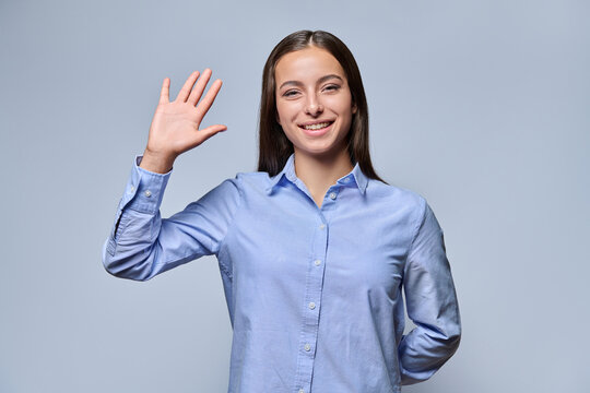 Smiling young woman waving hand greeting gesture studio shot