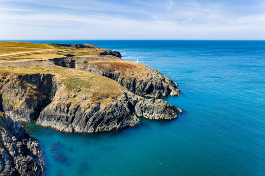 Rugged coastal cliffs and headlands overlooking blue sea water, footpath running along grassy cliff top under sunny skies, wide view