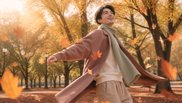 Joyful young Asian man with outstretched arms in autumn park. Happy male enjoying falling leaves on a sunny day