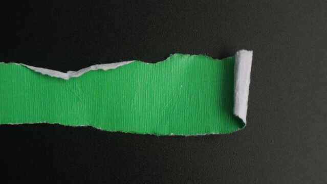 A strip of green paper torn from a black background with copy space.