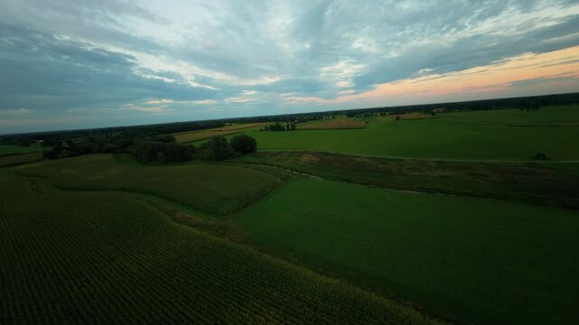 H&ouml;herer FPV-Drohnenflug &uuml;ber weite Wiesen und l&auml;ndliche Landschaft unter einem dramatischen, bew&ouml;lkten Abendhimmel