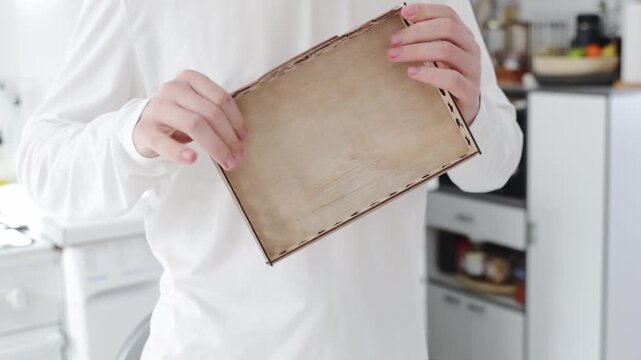 A young, unrecognizable Caucasian man stands at a table, snapping the side pieces into place, assembling a carved wooden tray for the Ramadan holiday. Close-up, side view with slow motion. Concept: tr