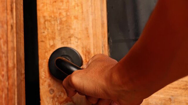 Close up of a hand holding the handle to open or close a wooden door, home entrance security and interior access concept.