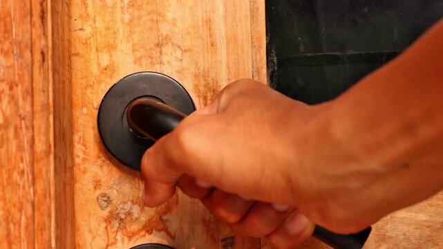 Close up of a hand holding the handle to open or close a wooden door, home entrance security and interior access concept.