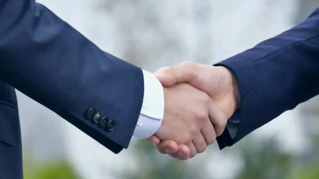 Two business people in suits shaking hands to finalize a deal outside