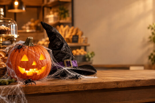 Halloween pumpkin with candle, cobwebs and witch hat on bakery counter, party decoration display concept