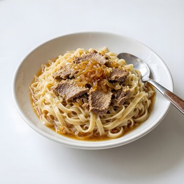 Savory beef noodle bowl with caramelized onions and rich jus sauce served on flat wheat noodles with a spoon side view