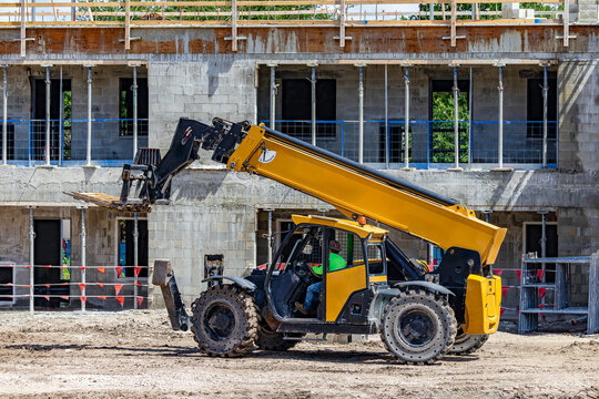 Yellow telescopic handler forklift parked on construction site with concrete block building in USA