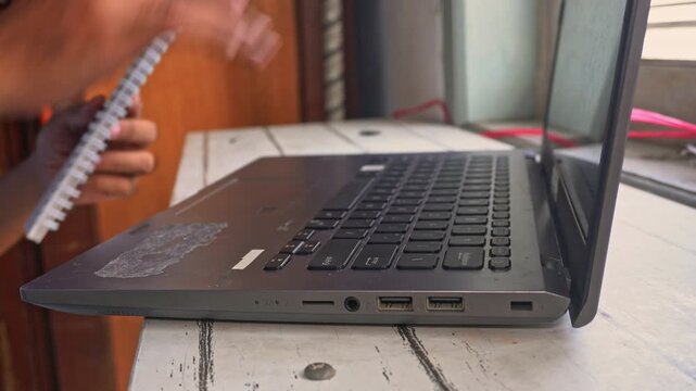Close up side angle view of male worker closing laptop and holding spiral notebook, tidying and organizing desk workspace after completing remote freelance job assignments.
