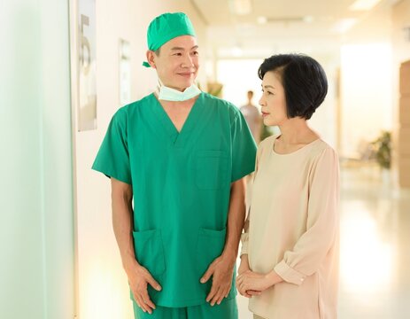 Japanese surgeon in green scrubs explaining to a family member in a bright hospital corridor