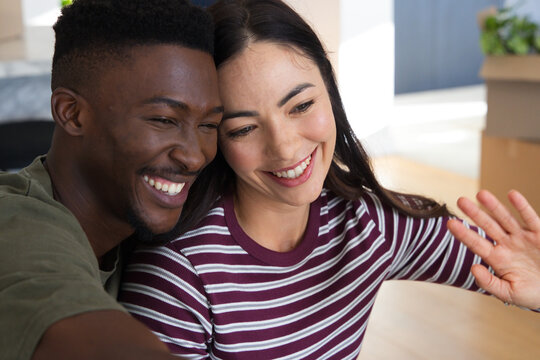 Diverse couple leaning smiling taking selfie at home with phone moving boxes maroon top olive tee