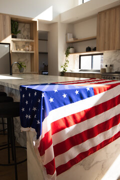United States flag cloth is draping over marble island near black faucet, sunlight casting folds