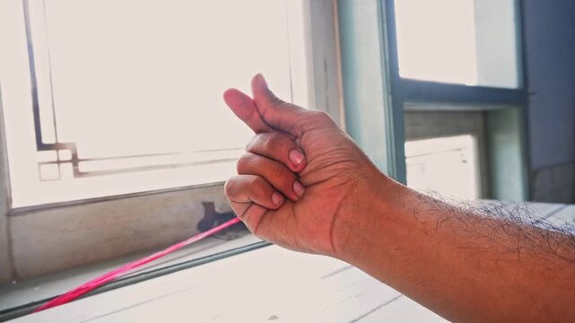 A male hand making a small heart gesture with fingers against a bright indoor window background showcasing a symbol of love and affection for a romantic connection or Valentine Day celebration