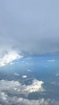 Aerial view of clouds and a faint rainbow visible above a landscape, showcasing the beauty of nature from an airplane window. Slow motion vertical footage, 4K, copyspace