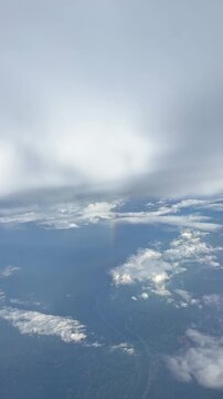 Aerial view of clouds and a faint rainbow visible above a landscape, showcasing the beauty of nature from an airplane window. Slow motion vertical footage, 4K, copyspace