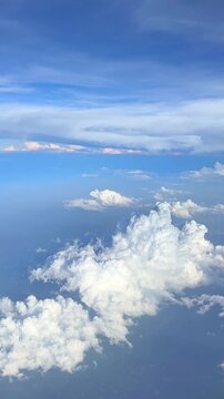 Expansive view of blue sky with fluffy white clouds and soft sunlight illuminating the atmosphere from an airplane window at high altitude. Slow motion vertical footage, 4K, copyspace