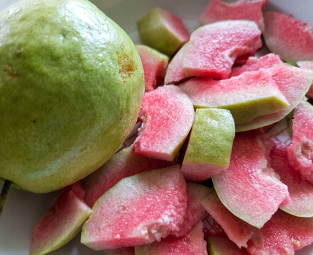 Fresh pink guava fruit, whole and sliced into pieces, close up view.