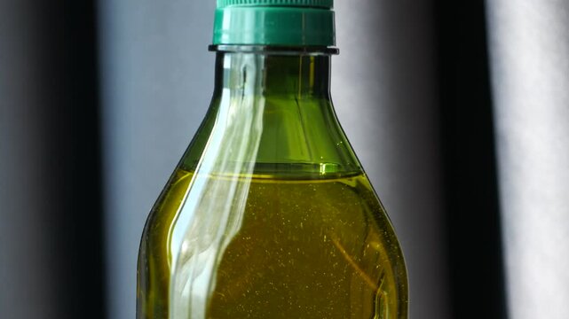 Bottle of extra virgin olive oil rotating on dark background with cinematic lighting and golden liquid motion